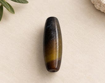 May include: A cylindrical bead with a smooth, polished surface featuring a gradient color transition from dark charcoal black at the top to a muted olive green in the center and a deep brown tone at the bottom, with a visible hole.