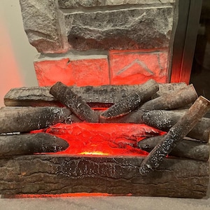 May include: An electric fireplace insert with faux logs and a glowing red ember bed. The logs are a dark brown with white accents, and the brickwork above is gray and textured.