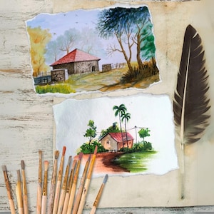 Op de afbeelding: Aquarel schilderijen van huizen met rode daken en bomen op gescheurd papier. Een grote veer en penselen staan ook in de afbeelding. De schilderijen hebben een rustiek, landelijk thema.