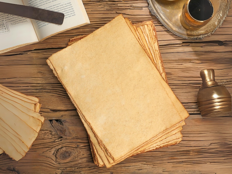 Op de afbeelding: Een stapel verouderde, cr&egrave;mekleurige papieren vellen met ruwe randen, gerangschikt op een rustiek houten oppervlak. Het papier heeft een vintage uitstraling, wat suggereert dat het gebruikt kan worden om te schrijven of voor artistieke doeleinden. Een metalen voorwerp en een decoratieve fles zijn ook zichtbaar.