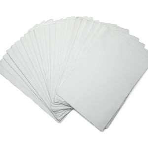 Op de afbeelding: Een waaier van blanco, witte rechthoekige kaarten, waarschijnlijk voor knutselen of briefpapier. De kaarten zijn opgestapeld en uitgespreid, waarbij hun schone, gladde oppervlak zichtbaar is. Ze liggen op een witte achtergrond.