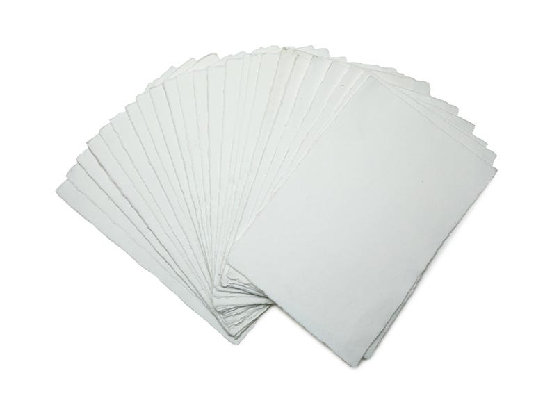 Op de afbeelding: Een waaier van blanco, witte rechthoekige kaarten, waarschijnlijk voor knutselen of briefpapier. De kaarten zijn opgestapeld en uitgespreid, waarbij hun schone, gladde oppervlak zichtbaar is. Ze liggen op een witte achtergrond.