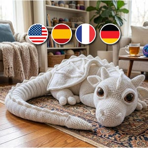 Pode incluir: Um grande peluche de dragão feito em crochê na cor branco sujo, com uma cauda longa segmentada, asas texturizadas e olhos castanhos proeminentes. A criatura é trabalhada com pontos detalhados, cabeça arredondada e pequenos chifres.