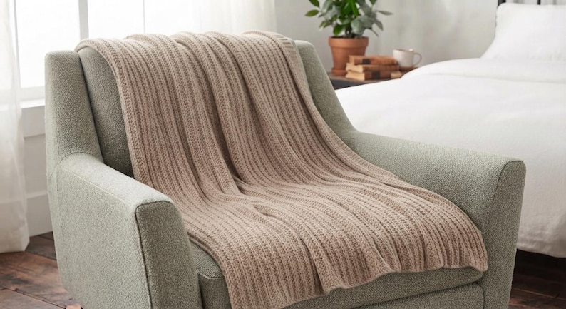 May include: A beige knitted throw blanket with a vertical ribbed texture draped over a light green upholstered armchair. The blanket features a consistent woven pattern throughout its length, providing a soft and textured appearance on the seat.