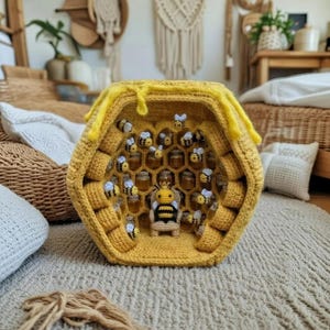 Puede incluir: Una exhibición de panal de abeja de ganchillo amarillo hecha a mano, con una abeja reina y varias abejas más pequeñas. Las celdas del panal contienen frascos en miniatura. La exhibición está sobre una alfombra de color neutro.