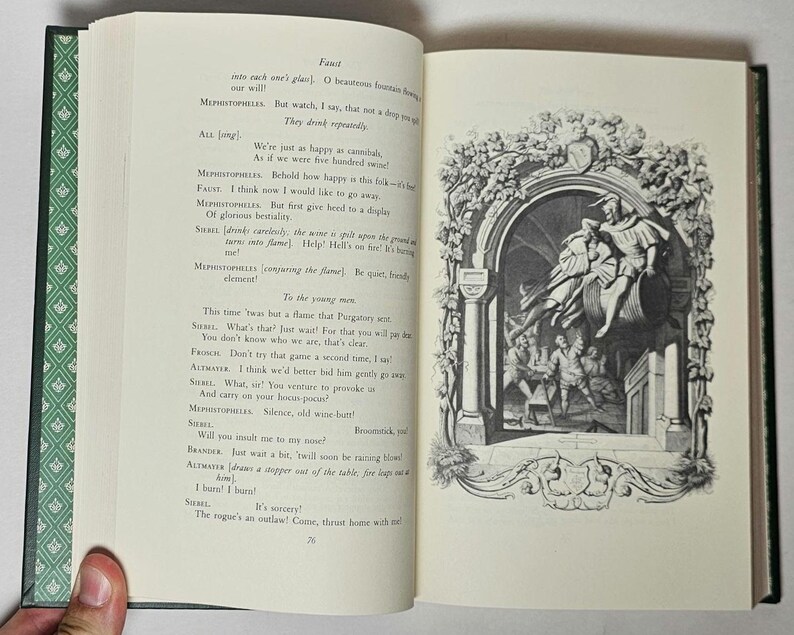 May include: Open book with text and a black and white illustration. The left page has printed text, while the right page features a detailed drawing of figures in an arched setting. The book has a green cover with a patterned design.