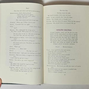 May include: Open book with text from a play, featuring pages with printed text in black ink. The book has a green cover with a decorative pattern and a hand is holding the book open.
