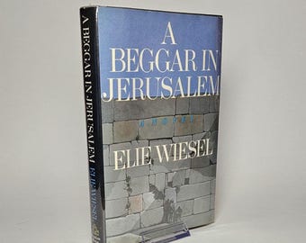 Puede incluir: Un libro azul y gris con el título "Un mendigo en Jerusalén" de Elie Wiesel. La portada muestra una pared de piedra con un pequeño grupo de personas caminando en la distancia.