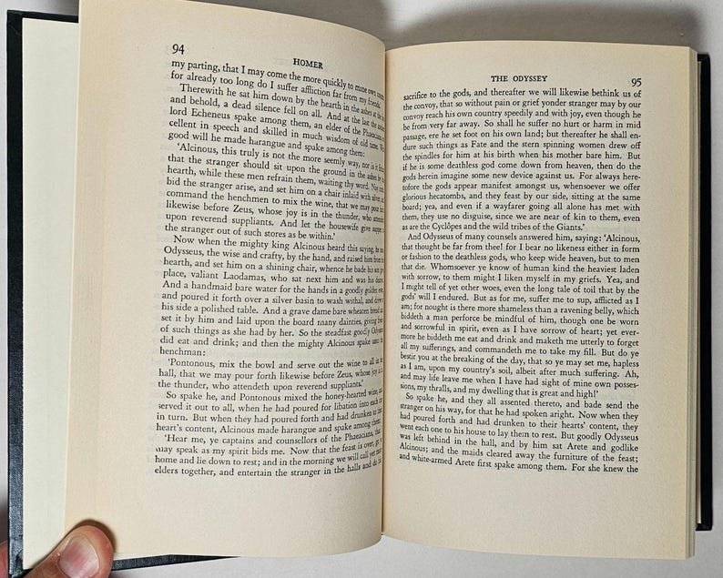 May include: Open book with text from Homer's Odyssey on cream-colored pages. The book is open to pages 94 and 95, with text in black font. The book has a black cover and is held by a hand.