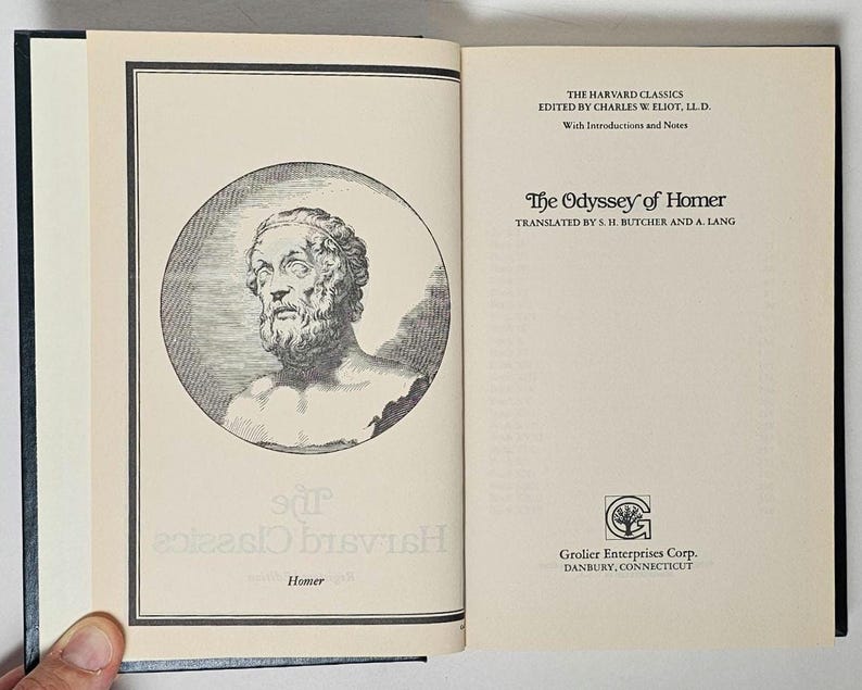 May include: Open book with black cover featuring a bust of a man in a circle on the left page. The right page displays the title "The Odyssey of Homer" and the text "The Harvard Classics" and "Grolier Enterprises Corp."