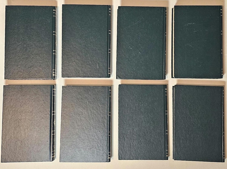 May include: Eight hardcover books with dark green covers are arranged on a light beige surface. The books are rectangular, with a textured appearance. The spines have gold accents. The books are likely part of a collection or set.