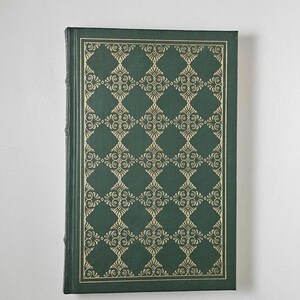 May include: A hardcover book with a dark green cover featuring a gold, ornate diamond pattern. The edges of the cover are also trimmed in gold. The book is closed and appears to be in good condition.