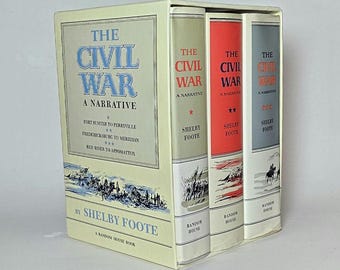 May include: A three-volume book set titled The Civil War: A Narrative by Shelby Foote, housed in a cream-coloured slipcase. The spines are cream, red, and grey, each featuring black text, star icons, and illustrations of soldiers in battle.