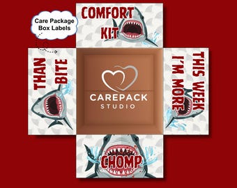 May include: A cardboard care package box with shark graphics and the text "COMFORT KIT", "THAN BITE", "CHOMP", and "THIS WEEK I'M MORE". The box features the "CAREPACK STUDIO" logo.