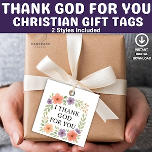 May include: A wrapped gift box with a white ribbon and a tag that reads "I THANK GOD FOR YOU." The tag features a floral wreath design with orange and purple flowers. The image also includes the text "THANK GOD FOR YOU CHRISTIAN GIFT TAGS."