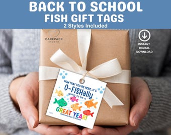 Op de afbeelding: Een ingepakt cadeau met een witte strik en een cadeaulabel. Het label luidt "O-FISHally going to be a GREAT YEAR!" met kleurrijke visillustraties. Bovenin staat de tekst "BACK TO SCHOOL FISH GIFT TAGS".