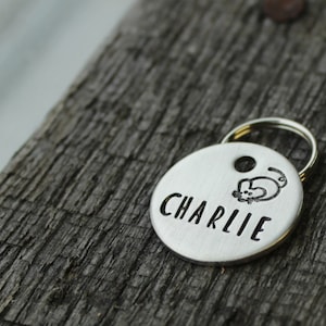 May include: Silver pet tag with a small cat illustration and the name "CHARLIE" engraved on it.