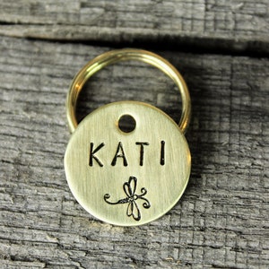 May include: Brass dog tag with a dragonfly design and the name "KATI" engraved on it.