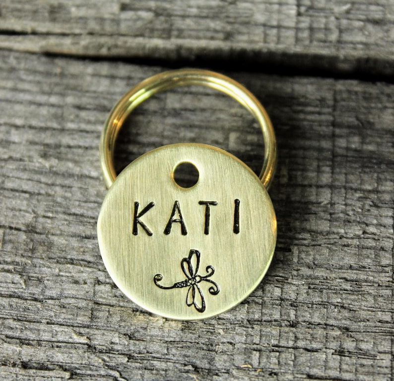 May include: Brass dog tag with a dragonfly design and the name "KATI" engraved on it.