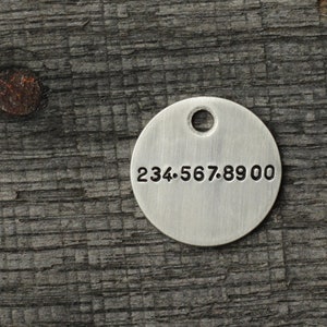 May include: A silver round tag with a hole at the top and the number 234.567.8900 engraved on the front.