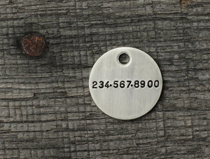 May include: A silver round tag with a hole at the top and the number 234.567.8900 engraved on the front.