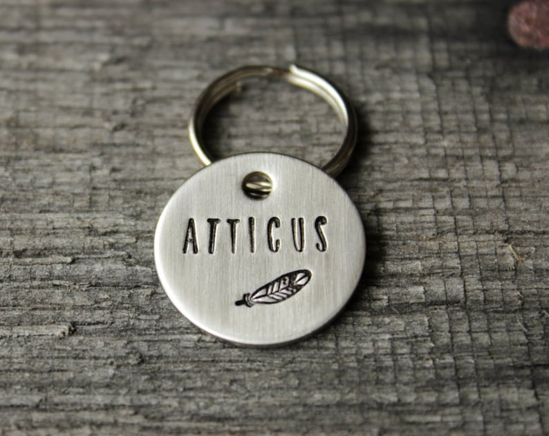May include: Silver dog tag with a feather design and the name "Atticus" engraved on it.