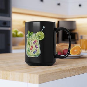 Peut inclure: Mug en céramique noire avec un motif de verre à cocktail. Le verre contient un liquide vert et des illustrations de bactéries colorées. Il est garni d'une tranche de citron vert et de menthe. Un bâtonnet argenté est inclus.