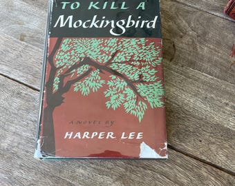 Könnte beinhalten: Ein Vintage-Hardcover-Buch mit dem Titel "To Kill a Mockingbird" von Harper Lee. Der Umschlag zeigt einen roten Hintergrund mit einer grünen Baumillustration.