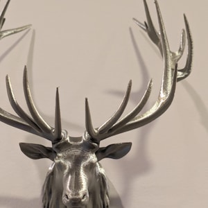May include: A silver 3D printed deer head with antlers mounted on a white wall.