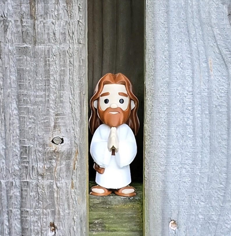May include: A figurine of Jesus with brown hair and a beard, wearing a white robe, and with hands clasped in prayer. The figurine is standing between two weathered wooden panels.
