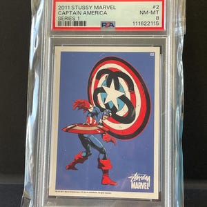 May include: A 2011 Stussy Marvel Captain America trading card, series 1, graded NM-MT 8. The card features Captain America with his shield. The card is in a protective plastic case.