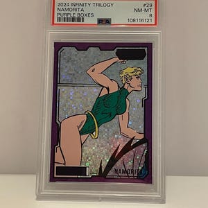 May include: A trading card featuring Namorita from the 2024 Infinity Trilogy series. The card has a purple border and a holographic background. The artwork depicts Namorita in a green bodysuit. The card is encased in a protective holder.