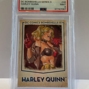 May include: A Harley Quinn trading card from the DC Bombshells Series 3, encased in a protective holder. The card features an illustration of Harley Quinn in a brown jacket, black top, and red gloves. The card is graded as Mint 9.