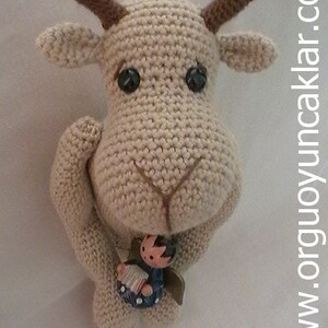 May include: A crocheted reindeer with brown antlers holding a small wooden figurine of a person playing an accordion. The reindeer is beige and has black eyes.
