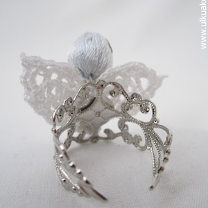 Puede incluir: Un &aacute;ngel de crochet blanco con un anillo de plata. El &aacute;ngel tiene una cabeza y alas de crochet blanco.