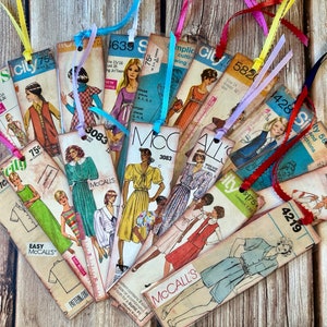 May include: A collection of vintage sewing pattern bookmarks with colorful ribbon ties. The bookmarks feature various sewing patterns, including dresses, shirts, and pants. The patterns are printed on paper with a vintage aesthetic.