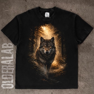 May include: Black t-shirt featuring a detailed illustration of a wolf in a forest setting. The wolf has brown and gray fur and is centered in the image. The background shows a forest with sunlight shining through the trees. The text "OLDERLAB" is printed vertically on the left side.