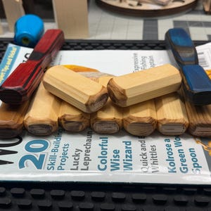 May include: A collection of wooden carving tools with various handle colors, including red, blue, and natural wood tones. The tools are arranged on a magazine with the title "Wood", featuring articles on carving projects. A blue object is in the background.