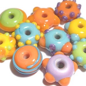 Peut inclure: Un ensemble de 10 perles en verre lampwork colorées avec un mélange de couleurs et de motifs. Les perles mesurent environ 8 mm de haut et 14 mm de large. Les perles ont un trou de 3/32 de pouce. Les perles sont présentées en deux arrangements : un tas de perles et une chaîne de perles.