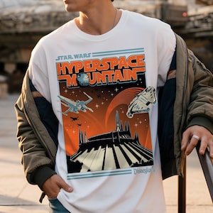 May include: White t-shirt featuring a Star Wars Hyperspace Mountain graphic. The design includes an orange and black mountain scene with spaceships and the text "Star Wars Hyperspace Mountain". The shirt is a classic crew neck.
