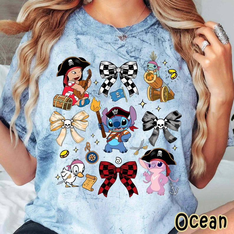 Może przedstawiać: Jasnoniebieska koszulka tie-dye z r&oacute;żnymi postaciami pirat&oacute;w z kresk&oacute;wek i wzorami kokard. Koszulka zawiera wizerunki Stitcha, kaczki i innych postaci w strojach pirackich, a także dekoracyjne kokardy.