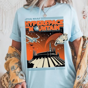 May include: Light blue t-shirt featuring a retro-style graphic for Star Wars: Hyperspace Mountain at Disneyland. The design includes the text "Hyperspace Mountain" and images of the Death Star, X-wing fighters, and the Millennium Falcon.