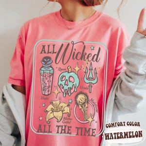 May include: A pink Comfort Color t-shirt with a graphic that says "ALL Wicked ALL THE TIME." The graphic features illustrations of villains and their symbols, including a poison bottle, skull, trident, and flower.