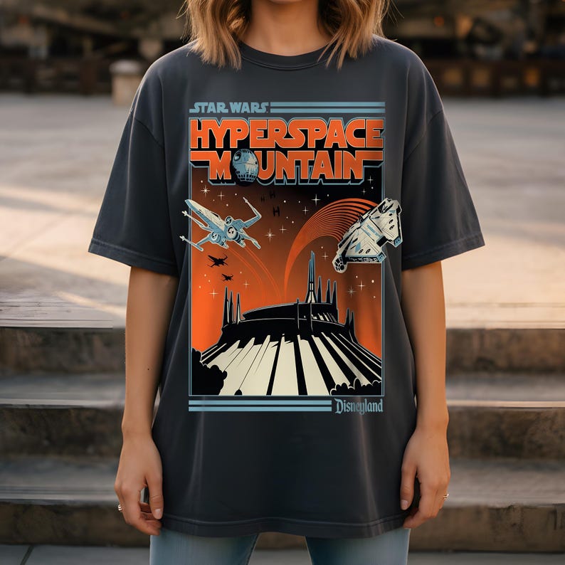 May include: Dark gray t-shirt featuring a Star Wars Hyperspace Mountain graphic. The design includes an X-wing fighter, the Millennium Falcon, and the Disneyland logo. The graphic is in shades of orange, blue, and white.