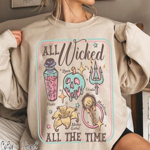 May include: Sand-colored sweatshirt with a graphic design featuring the text "ALL Wicked ALL THE TIME." The design includes illustrations of a poison bottle, skull, trident, flower, and other elements, with character names.