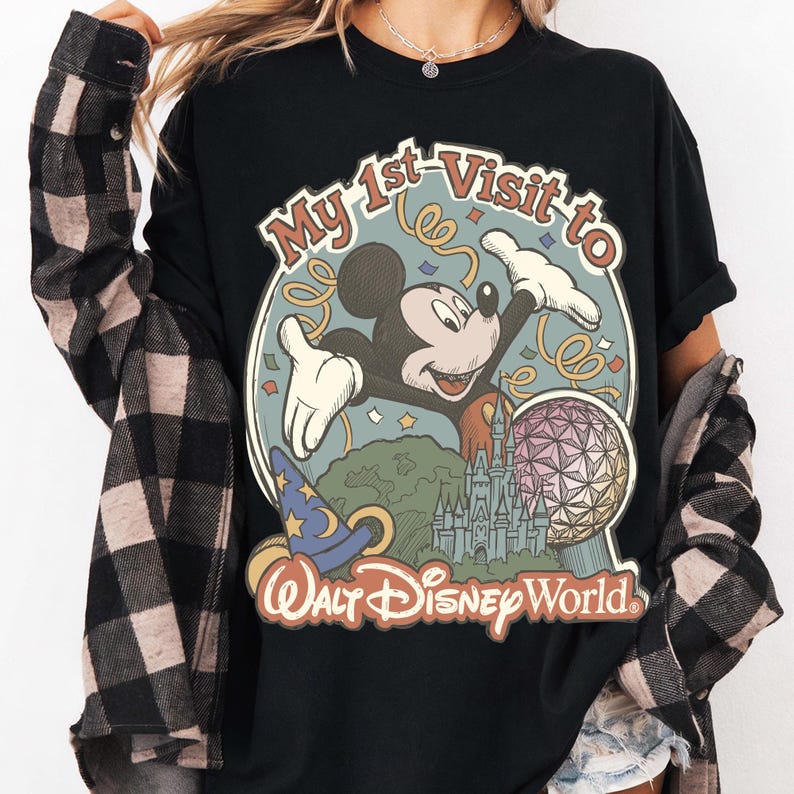 May include: Black t-shirt featuring a graphic of Mickey Mouse with the text "My 1st Visit to Walt Disney World." The design includes a castle, a sorcerer's hat, and a geodesic sphere. The shirt has a vintage, retro style.