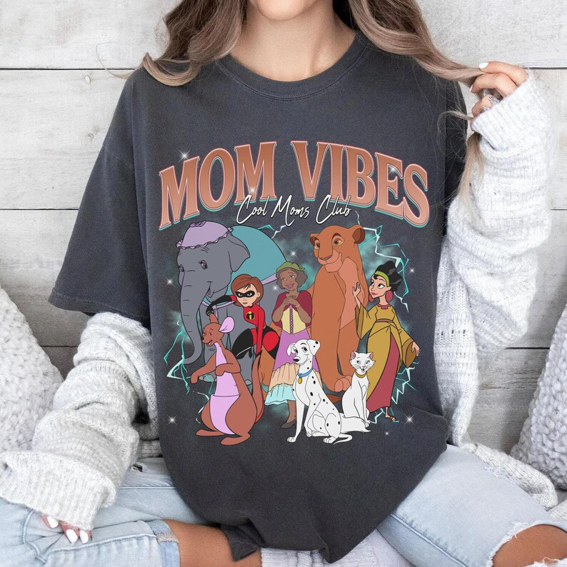 May include: A dark gray t-shirt with the text "MOM VIBES Cool Moms Club" in pink and orange letters. The shirt features a graphic of Disney characters including Dumbo, Simba, and a kangaroo.