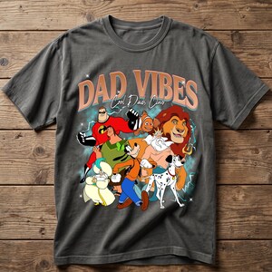 Puede incluir: Camiseta gris con un gr&aacute;fico de personajes de dibujos animados y el texto "DAD VIBES Cool Dads Club". El dise&ntilde;o incluye personajes como Mr. Incre&iacute;ble, Simba y Goofy. La camiseta est&aacute; hecha de un material suave.