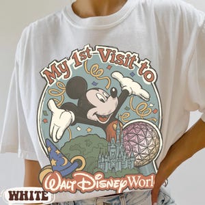 May include: White t-shirt featuring a colorful graphic of Mickey Mouse with the text "My 1st Visit to Walt Disney World." The design includes a castle, a sphere, and a wizard hat. The word "WHITE" is printed at the bottom.