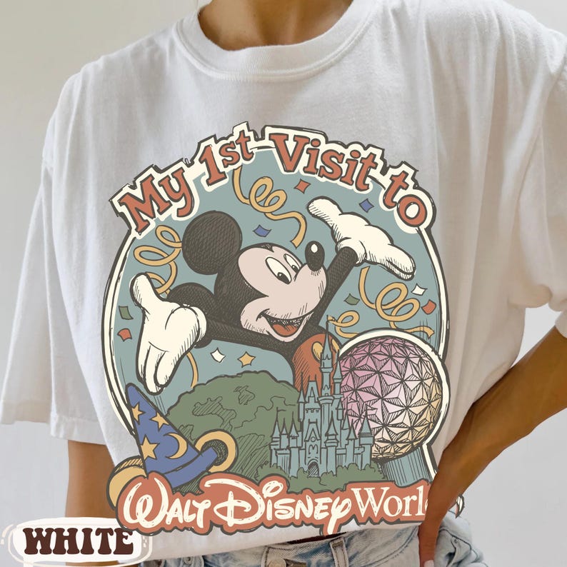 May include: White t-shirt featuring a colorful graphic of Mickey Mouse with the text "My 1st Visit to Walt Disney World." The design includes a castle, a sphere, and a wizard hat. The word "WHITE" is printed at the bottom.